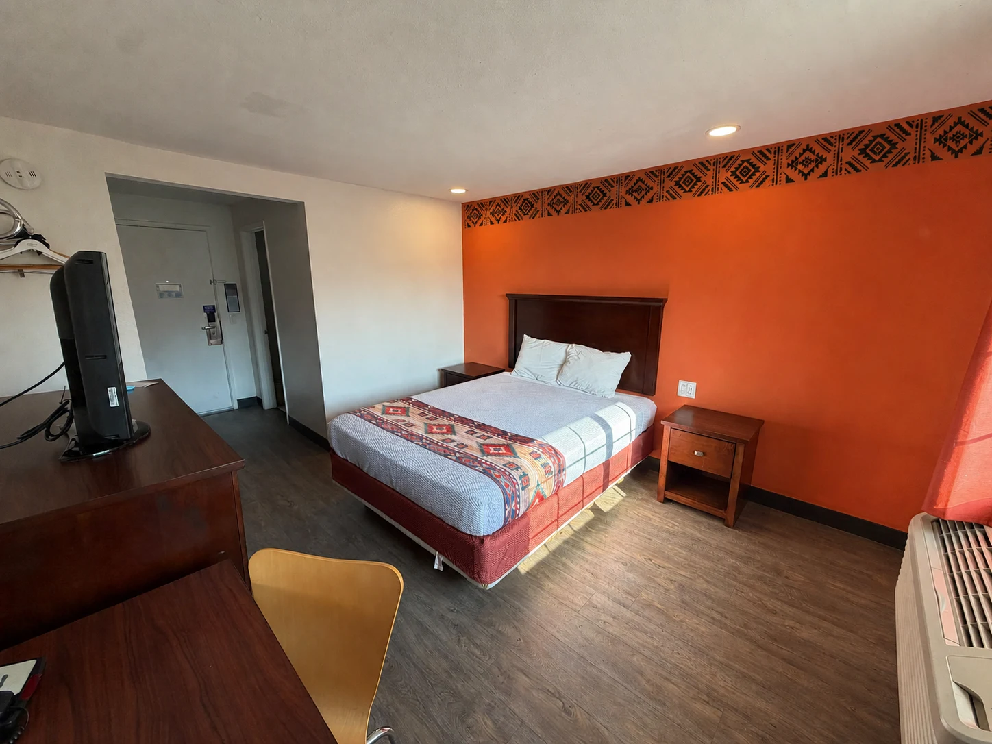 Mobility-accessible queen room with a hand-painted geometric border on the orange accent wall